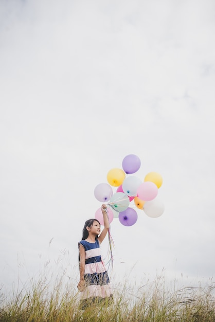 Маленькая девочка, играя с воздушными шарами на поле лугов.
