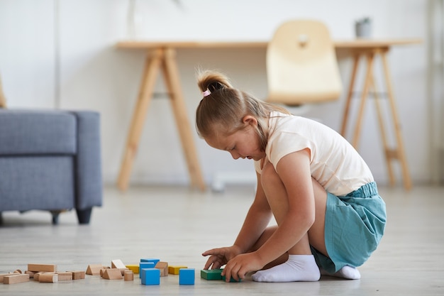 Little girl playing with blocks while sitting on the floor in the living room at home