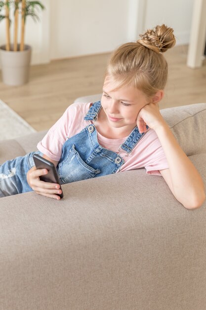 Bambina che gioca con un telefono cellulare a casa su uno strato