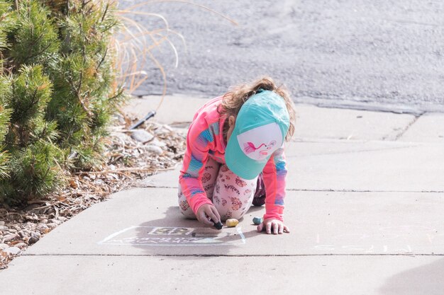 Little girl playing with chalk on a driveway in front of the house.