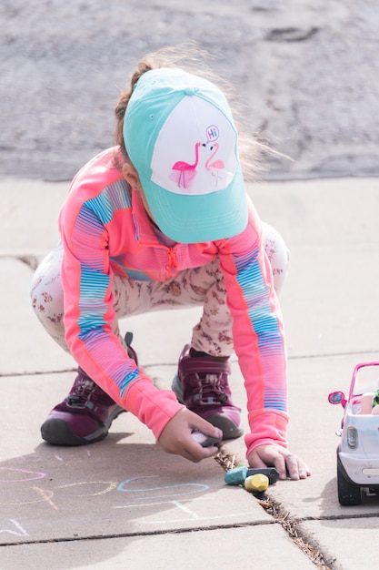 Little girl playing with chalk on a driveway in front of the house.