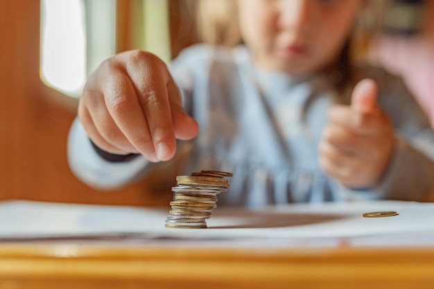 Little girl playing with coins making stacks of money First lessons in finance Accumulation Credit kid saving money for the future concept