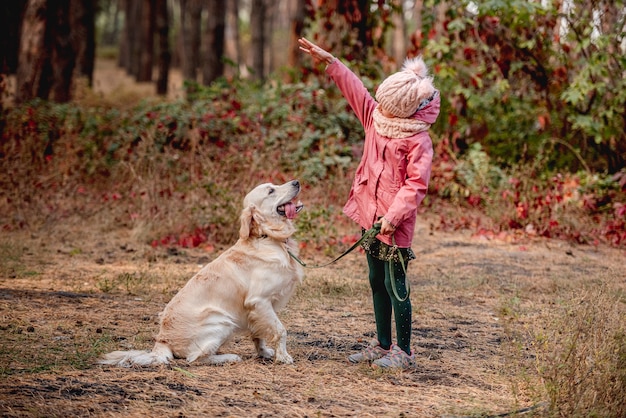 Маленькая девочка играет с собакой золотистого ретривера на красочной осенней природе