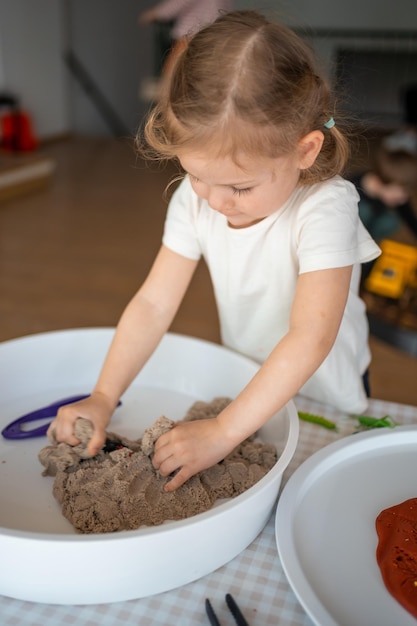 Фото Маленькая девочка играет с кинетическим песком и игрушками-насекомыми. сенсорное развитие и тематические занятия с детьми. развитие мелкой моторики.