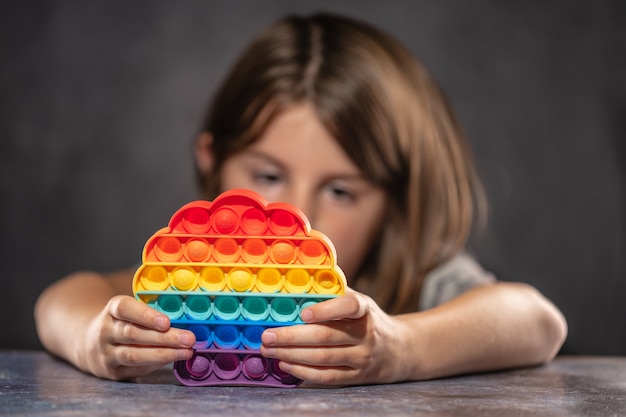 Foto bambina che gioca con il giocattolo antistress in silicone pop it color arcobaleno.