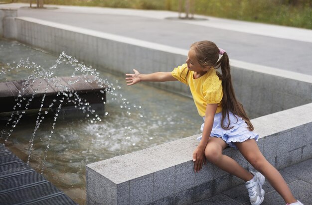 little girl playing with small fountains in the town square on a hot summer day