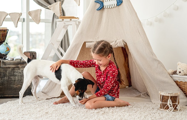 Little girl playing with smooth fox terrier dog at home