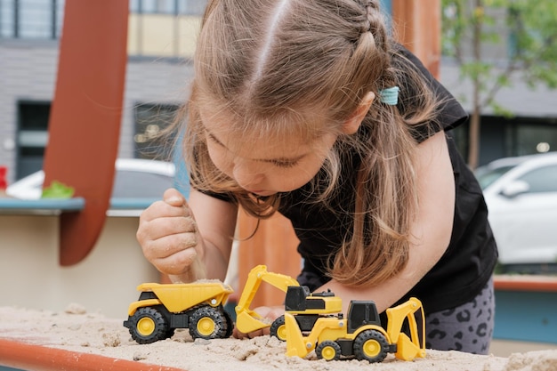 Bambina che gioca con i camion giocattolo in sandbox all'aperto