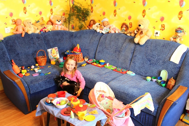 Маленькая девочка играет с игрушками и кошкой в своей комнате