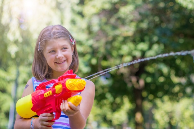 Bambina che gioca con la pistola ad acqua nel parco in una giornata di sole