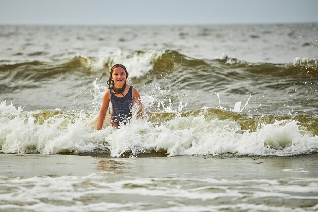 写真 小さな女の子が海で波で遊んでいます子供が遊びながら波でスプラッシュしています子供が海でジャンプしています