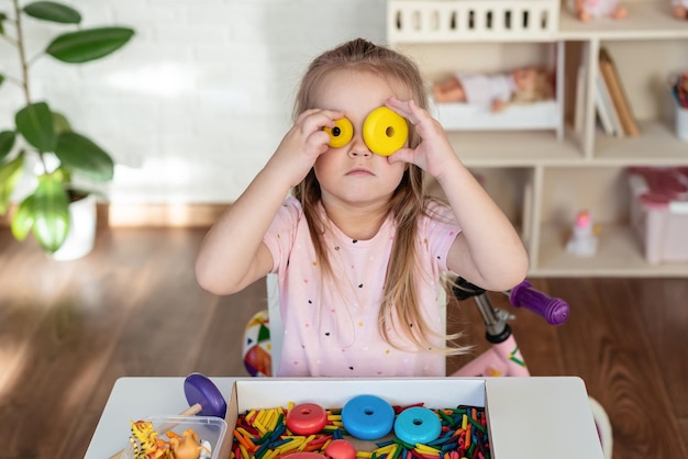 A little girl playing with wooden pyramid and colored dyed pasta Sensory play and learning colors activity for kids material Montessori games for fine motor skills sensory bin educational toy