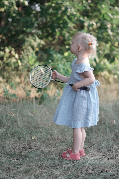 Little girl plays badminton outside Fulllength portrait of child in blue sundress with racket in her hands Vertical frame