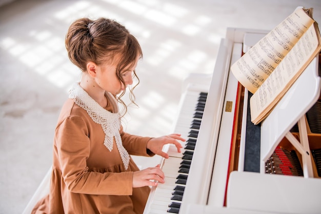 어린 소녀는 밝고 햇볕이 잘 드는 방에서 큰 흰색 피아노를 연주합니다