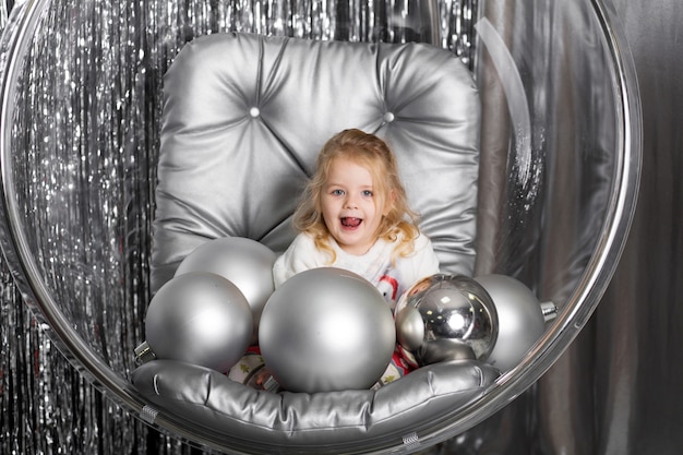 Little girl plays in a chair a glass bowl with silver balls.