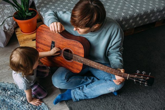 Little girl plays the guitar with her mother on the floor at home