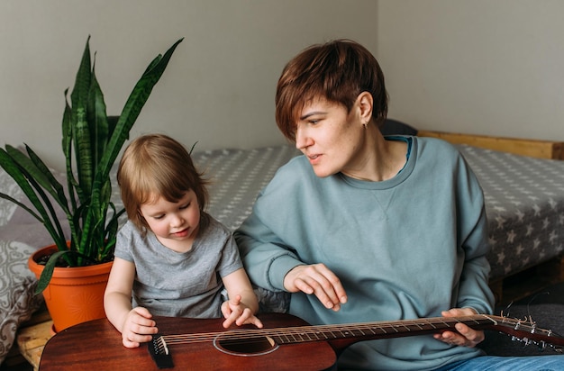 Маленькая девочка играет на гитаре со своей матерью дома на полу