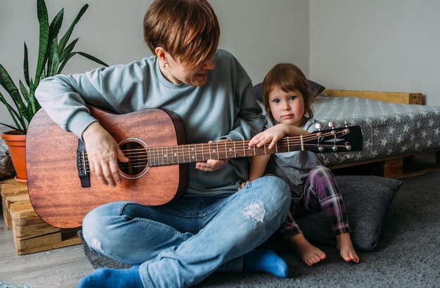 Маленькая девочка играет на гитаре со своей матерью на полу дома.