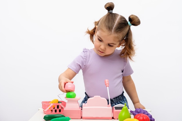 La bambina gioca nel negozio scansiona e pesa le verdure su bilance giocattolo, primo piano del registratore di cassa per bambini, concetto di giochi domestici per bambini