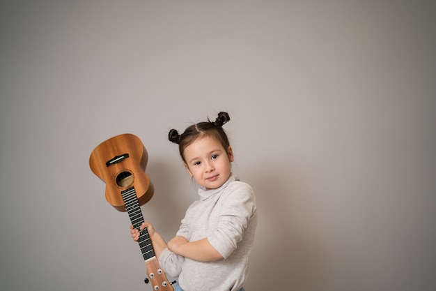 Little girl plays ukulele. Creative development in children. Musical education from childhood. Teaching music online at home.