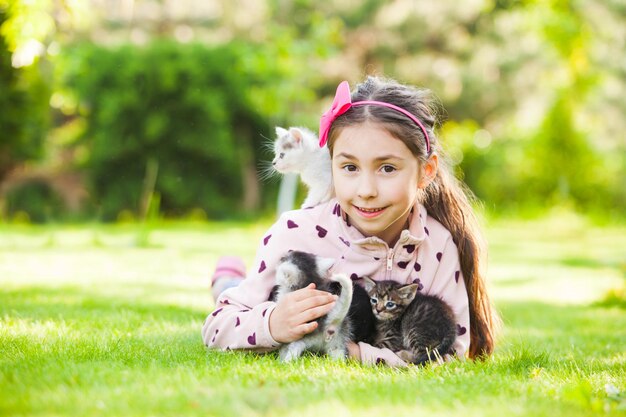 Little girl plays with kittens on green grass in garden at sunny day