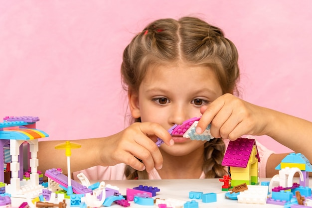 A little girl plays with plastic cubes on a pink.