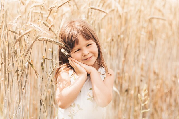 A little girl plays with spikelets in a wheat field