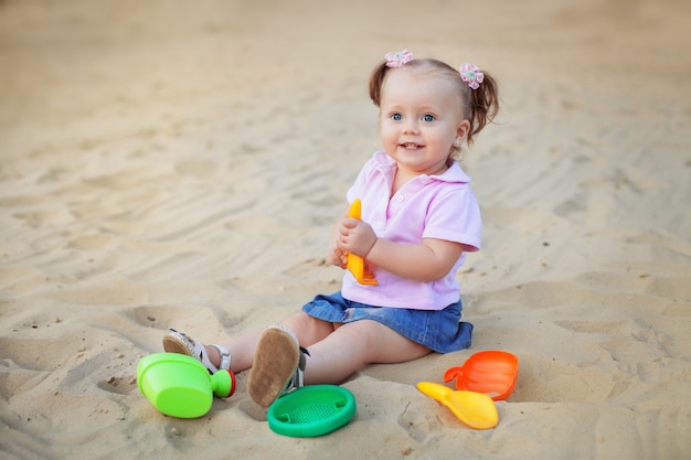 어린 소녀는 모래에 장난감으로 재생합니다.