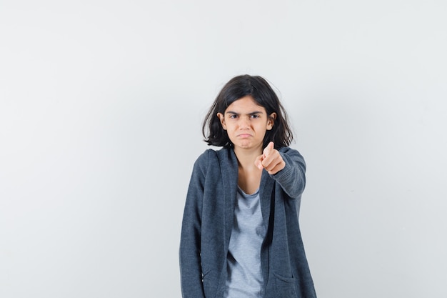 Little girl pointing at camera in t-shirt, jacket and looking offended. front view.