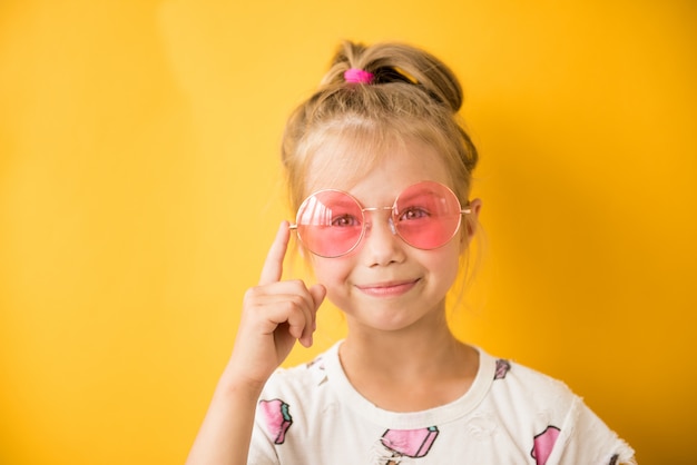 Little girl pointing finger at pink glasses on yellow