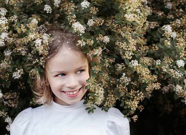 Little girl portrait with long blond hair, close up, flowering bush. Spring time concept.