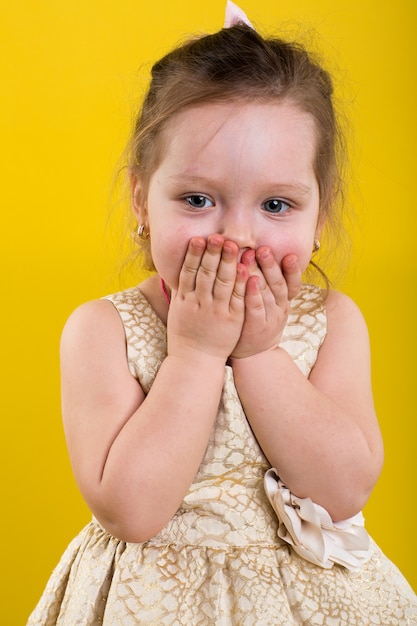 Little girl poses in beautiful dress on yellow background