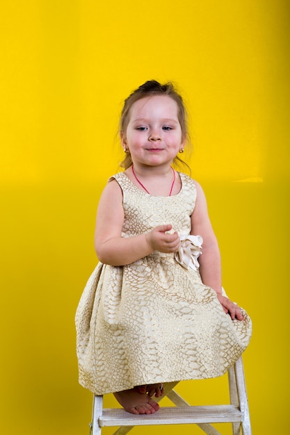 Little girl poses in beautiful dress on yellow background