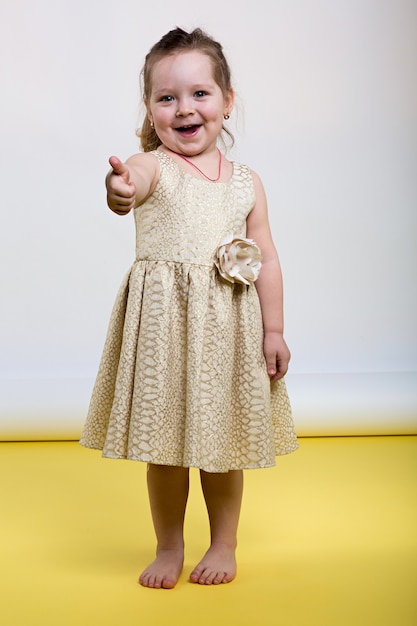 Little girl poses in beautiful dress on yellow floor