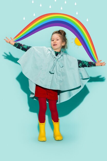 Little girl posing in fashion style wearing autumn clothing on blue background. Rubber yellow boots.