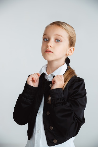 Little girl posing in school's uniform with backpack on white wall