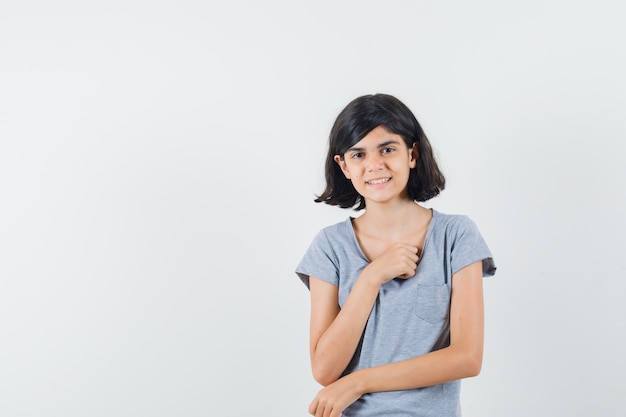 Little girl posing while standing in t-shirt and looking optimistic , front view.