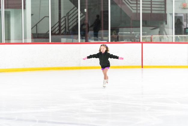 Little girl practicing figure skating on an indoor ice skating rink.