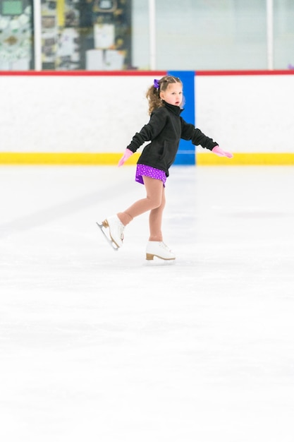 Foto bambina che pratica pattinaggio artistico su una pista di pattinaggio sul ghiaccio al coperto.