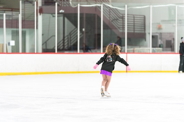 Foto bambina che pratica pattinaggio artistico su una pista di pattinaggio sul ghiaccio al coperto.