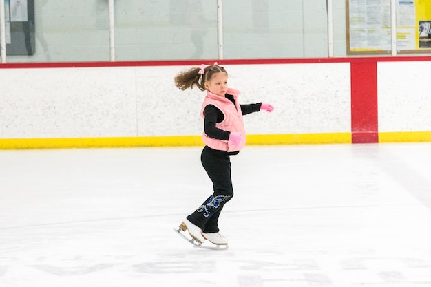 Photo little girl practicing figure skating moves on the indoor ice rink.