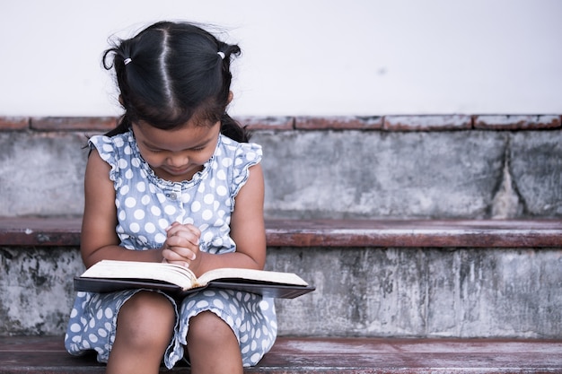 Little girl prays with a Holy Bible