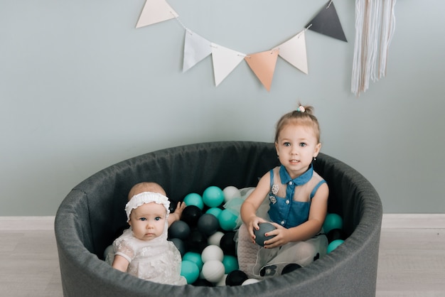 就学前の小さな女の子と彼女の妹がカラフルなプラスチックボールでプールで遊んで