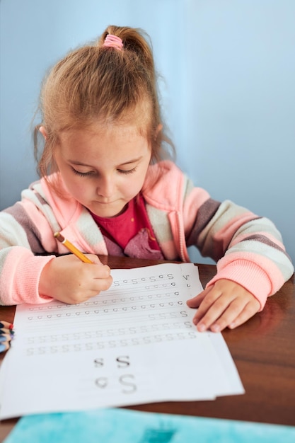 Фото Маленькая девочка в дошкольном возрасте учится писать письма в школе. ребёнок пишет письма, делая школьную работу.