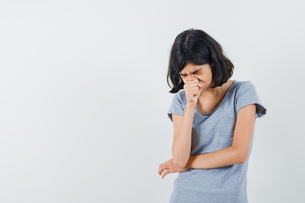 Little girl pressing fist on nose in t-shirt and looking pensive. front view.