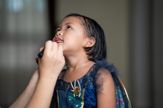 A little girl in a princess costume paints a red lipstick.