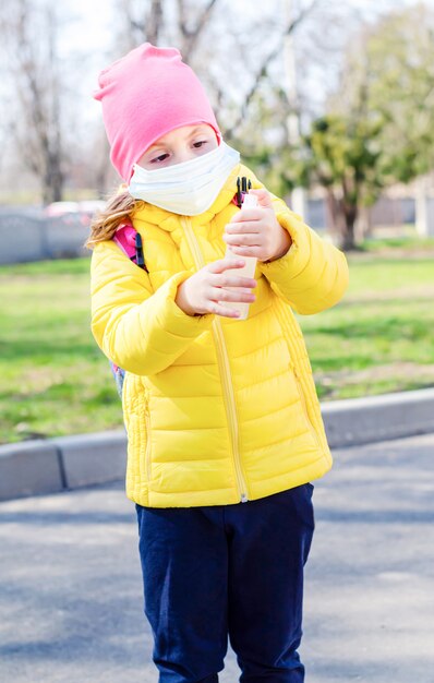 防護マスクの少女は、手の消毒剤を手に持っています。