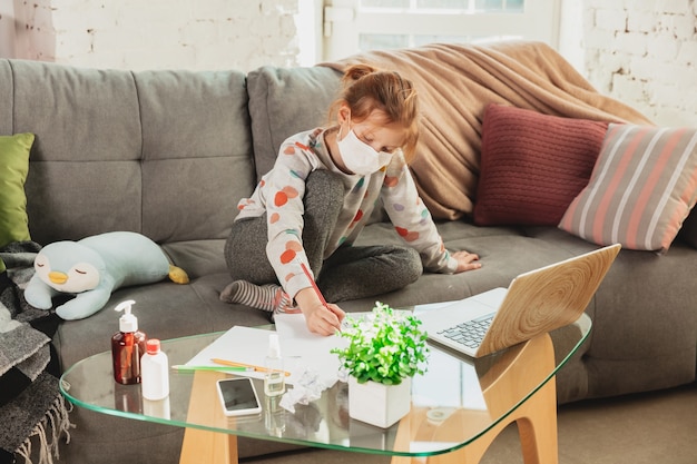 Little girl in protective mask isolated at home with coronavirus respiratory symptoms such as fever, headache, cough in mild condition. Healthcare, medicine, quarantine, treatment concept. Feels sick.