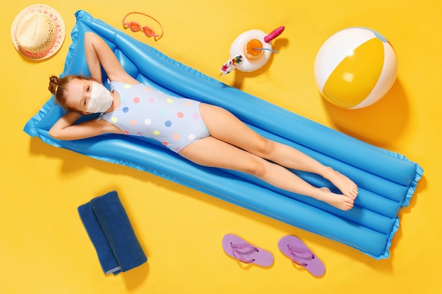 Little girl in a protective mask lies on a mattress