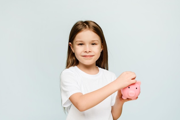 A little girl puts a coin in a piggy bank The concept of teaching children personal finance